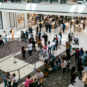 A bustling shopping center with a large crowd queuing inside an Apple Store.