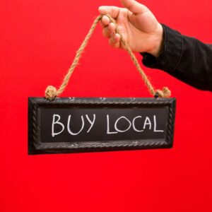 Person holding a 'Buy Local' sign suspended on ropes, promoting local business.